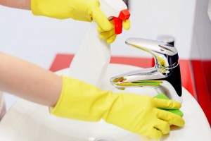 Close up of female hands with rubber gloves spraying liquid detergent on tap and cleaning it with sponge. Spring cleaning